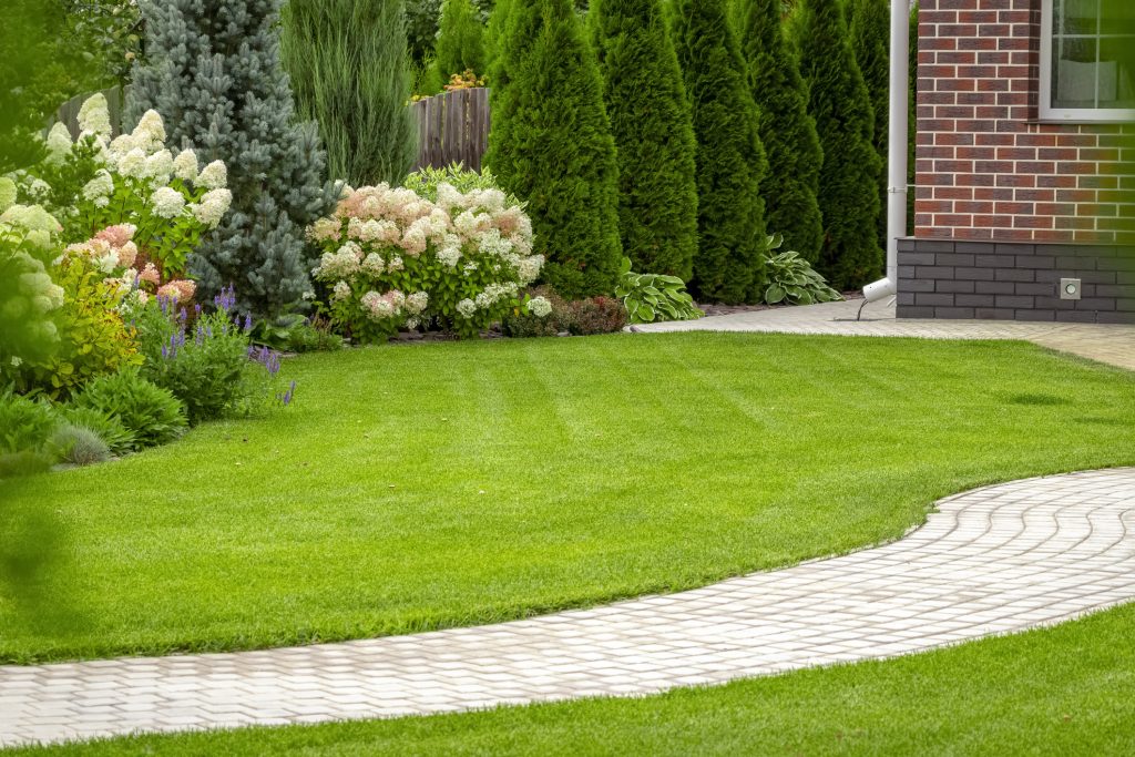 A beautifully mowed lawn edged in flowering plants and dissected by a tiled path creates a welcoming environment for guests and the homeowners alike.